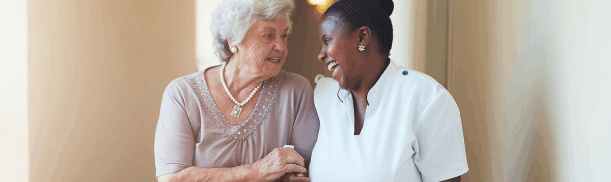 a care professional walking with an older adult in a hallway, providing one-to-one care support