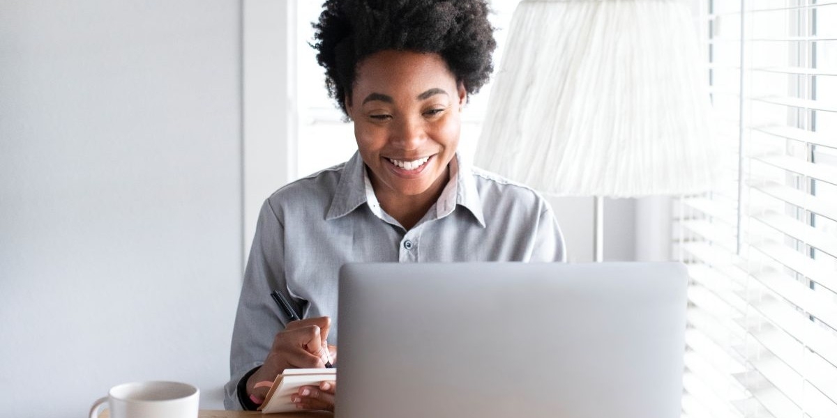 Liaison Care - Postgraduate Diploma In Continuing Healthcare - Blog Post 1 A woman sitting at a desk using her laptop and writing notes, participating in continuing healthcare postgraduate diploma